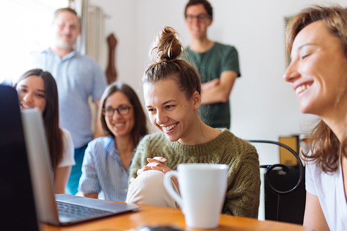 Equipo compartiendo y sonriendo alrededor de un computador